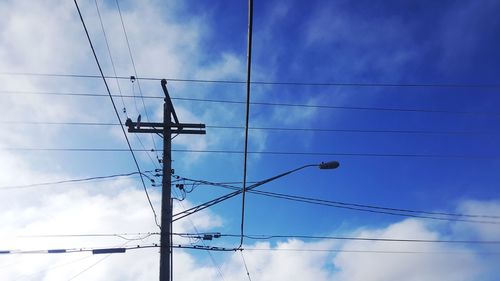 Low angle view of electricity pylon against blue sky