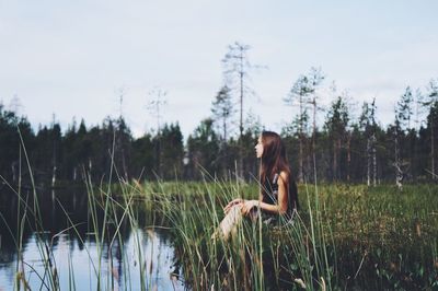 Young woman sitting on grass against trees