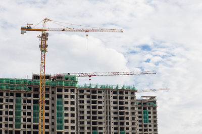 Low angle view of crane at construction site against sky