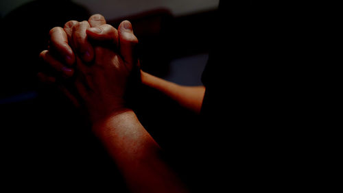 Midsection of person with hands clasped in dark