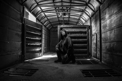 Man wearing mask while kneeling in corridor