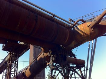 Low angle view of large rusty pipes in steel mill against sky