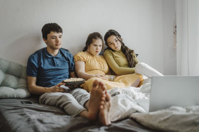 Down syndrome woman watching movie on laptop while sitting with siblings on bed at home