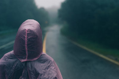 Rear view of man wearing raincoat standing on road