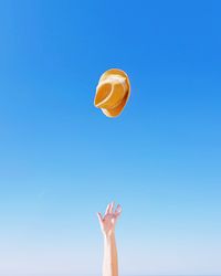 Cropped image of hand throwing hat against clear blue sky