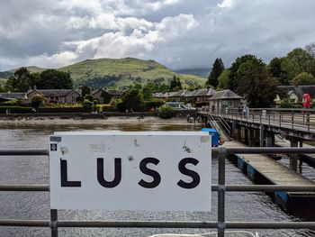 Text on railing by river against sky