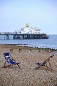 Two empty deckchairs facing each other on desserted shingle beach with pier in background