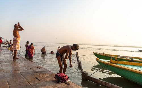 People on beach against clear sky during sunset