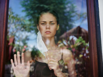 Portrait of young woman looking through window