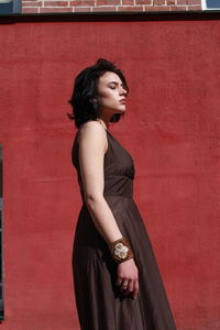 Beautiful woman in brown dress standing against red wall