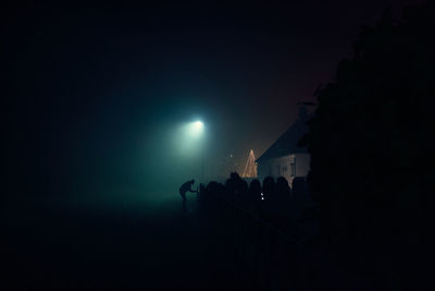 Silhouette people on illuminated street against sky at night