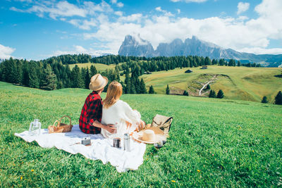 Rear view of couple sitting on field against sky