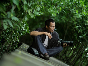 Young man looking down while sitting on tree