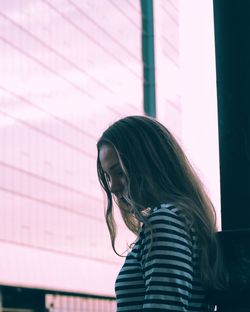 Side view of young woman leaning on pole against building