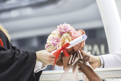 Cropped hands of people holding diploma and bouquet at college campus