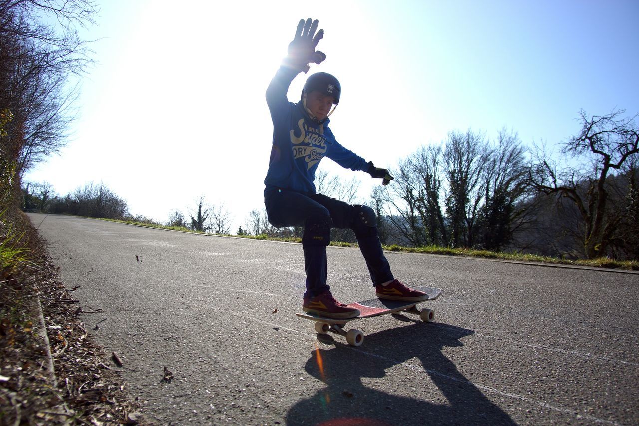 full length, tree, lifestyles, jumping, clear sky, leisure activity, skateboard, road, mid-air, skateboarding, casual clothing, balance, transportation, sunlight, street, day, human representation, standing