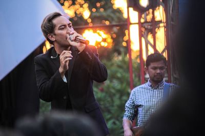 Young man holding camera while standing in illuminated park