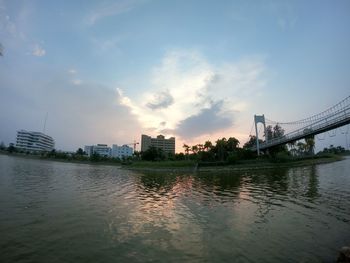 Bridge over river by buildings against sky during sunset