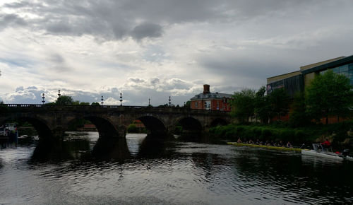 Bridge over river by buildings against sky