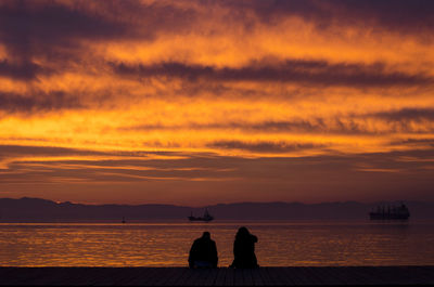 Silhouette people by sea against sky during sunset