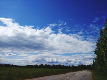 Empty road amidst field against sky