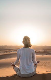 Rear view of woman sitting on sand in desert