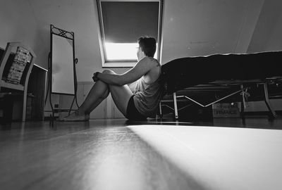 Side view of man sitting by bed at home