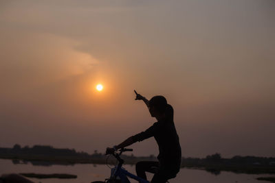 Silhouette man riding bicycle on shore against sky during sunset