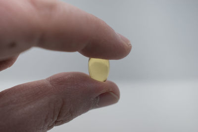 Close-up of hand holding yellow leaf against white background