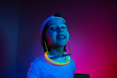 Cyberpunk boy child in white t shirt and sunglasses neon sticks on neck listening music on wall