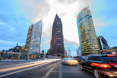 Cars on road by buildings against sky in city