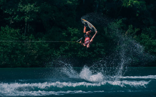 Man surfing in sea against trees