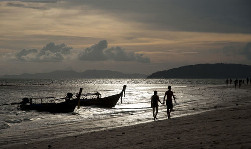 Silhouette couple walking on shore at beach against sky during sunset