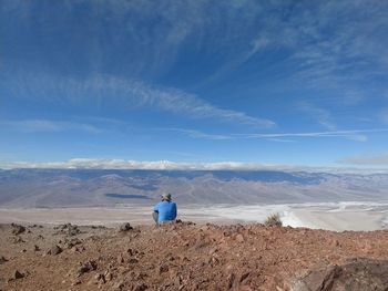 Rear view of man sitting on landscape against blue sky