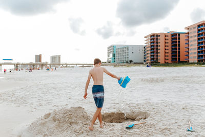 Full length of shirtless boy on beach against sky