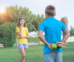 Teenage boy and girl with apple and burger in the park. choice between healthy and unhealthy food.