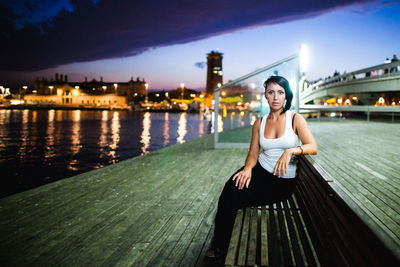 Woman sitting on bridge over river in city against sky