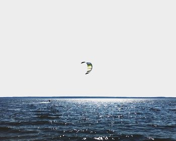 Person paragliding over sea against clear sky