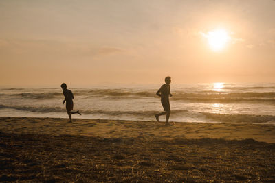 Silhouette two man run on beach with sunrise and sea background