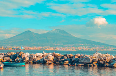 View of mount vesuvius and the gulf of naples with rocks and blue boat. naples, italy