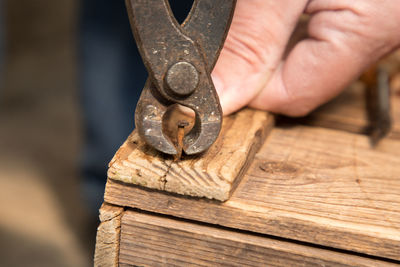 Close-up of man hand removing rusty nail from wood at workshop