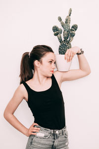 Young woman with potted plant and hand on hip standing against white background