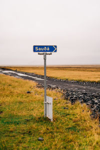 Road sign on field against sky