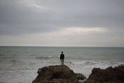 Rear view of man standing on rock by sea against sky