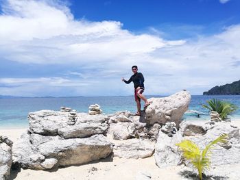 Man standing on rocks by sea against sky