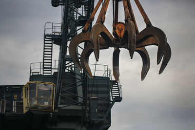 Low angle view of scrap metal and crane against sky