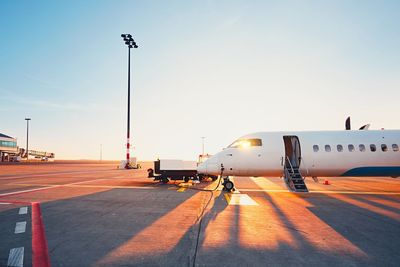 Airplane on airport runway against sky during sunset