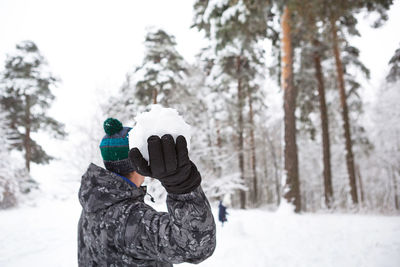 A young man with a snowball in his hand is having fun, swinging for a throw. 