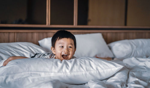 Portrait of little boy with happy smiley face is lying down on the bed at home, warm and cozy scene.