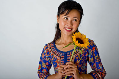 Woman with sunflower looking away against gray background